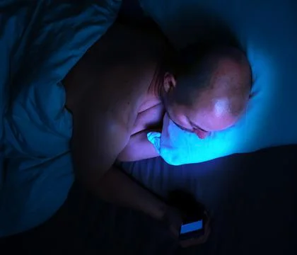 Man using his phone in bed at night with harmful blue light. 스톡 사진