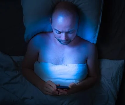 Man using his phone in bed at night . Stock Photos