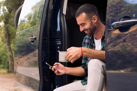 Man using his phone sitting in the door of his van Stock Photos