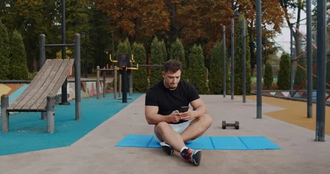 A man is using his phone while performing exercises at an outdoor gym Video stock 317979275