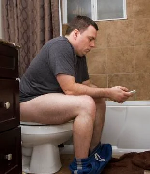Man using his phone while using the bathroom Stock Photos