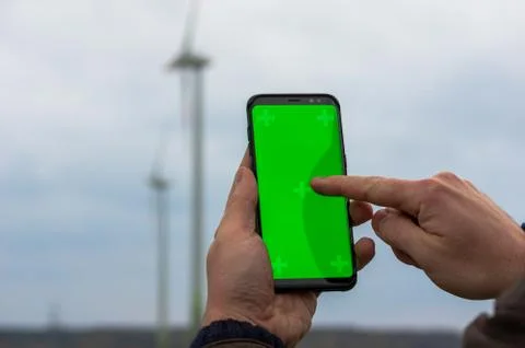 Man using his smartphone in front of out of focus wind turbines 写真素材