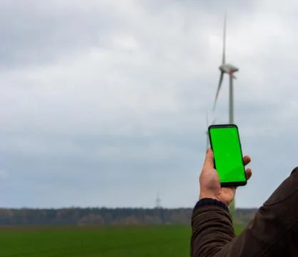 Man using his smartphone in front of out of focus wind turbines Stock Photos