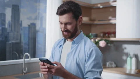 A man is using his smartphone in a modern kitchen that offers a beautiful city Stock Footage 316037863