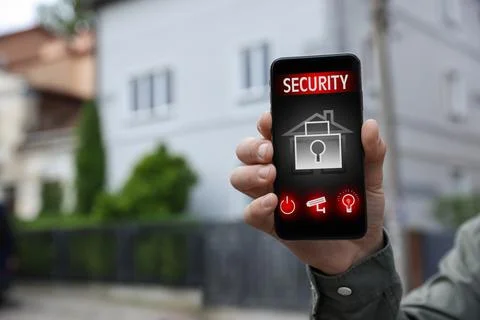 Man using home security application on smartphone in front of house outdoors, Foto stock