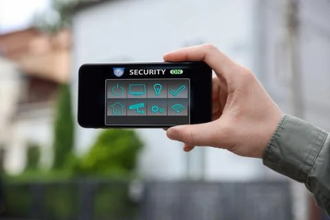 Man using home security application on smartphone in front of house outdoors, 스톡 사진