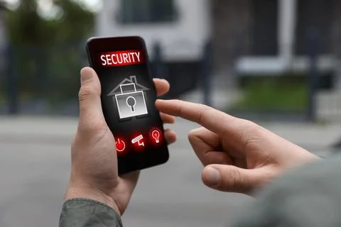 Man using home security application on smartphone in front of house outdoors, Stock Photos