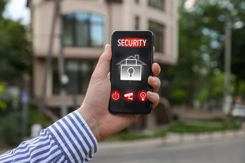 Man using home security application on smartphone in front of house outdoors, Stock Photos