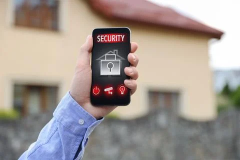Man using home security application on smartphone in front of house outdoors, Foto stock