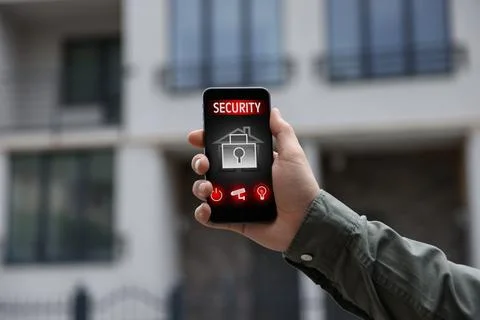 Man using home security application on smartphone in front of house outdoors, Stock Photos