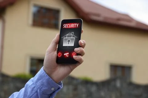 Man using home security application on smartphone in front of house outdoors, Stock Photos