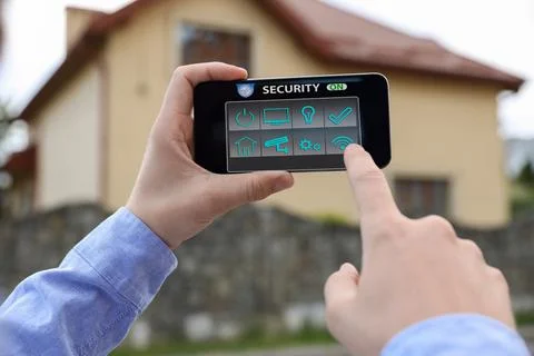 Man using home security application on smartphone in front of house outdoors, Foto stock
