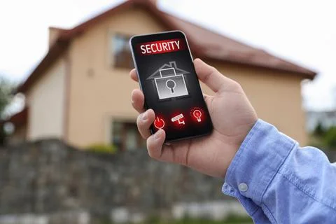 Man using home security application on smartphone in front of house outdoors, Stock Photos