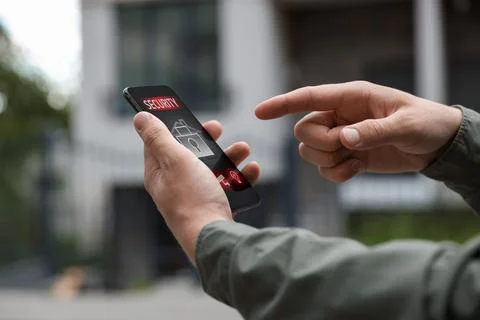 Man using home security application on smartphone in front of house outdoors, Stock Photos