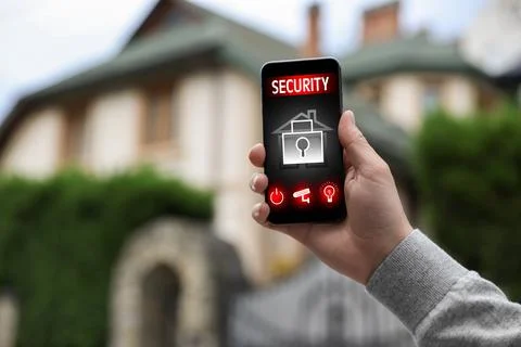 Man using home security application on smartphone in front of house outdoors, Stock Photos