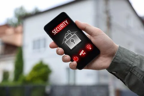 Man using home security application on smartphone in front of house outdoors, Stock Photos
