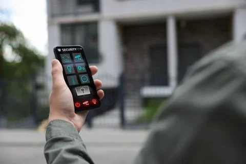 Man using home security application on smartphone in front of house outdoors, Stock Photos