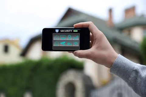 Man using home security application on smartphone in front of house outdoors, Foto stock