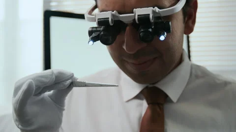 Man Using Illuminated Magnifying Glasses and Tweezers to Inspect Tiny Gemstones Stock Footage 310121747
