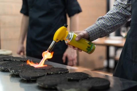 Man using a kitchen torch to make buns more crispy Stock Photos