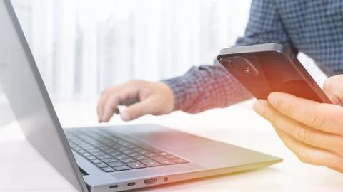 A man is using a laptop and a cell phone Stock Photos