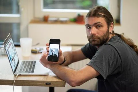 Man using laptop and displaying a picture on his cellphone while taking a short Stock Photos