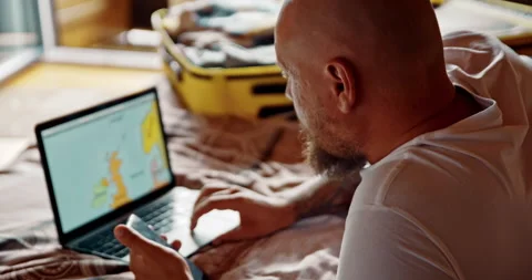 Man using laptop and smartphone planning vacation. Organizing trip after packing Stock Footage 141566070