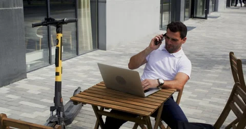 Man using laptop and smartphone at outdoor cafe, remote work Stock Footage 329187096