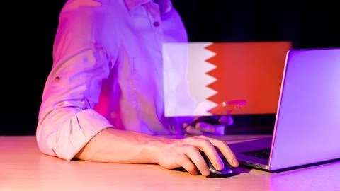Man using laptop and smartphone with Bahrain flag projection in neon lighting Foto stock