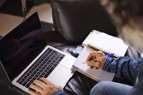 Man using laptop and writing notes in a notebook and on the sofa at home. Tel 스톡 사진