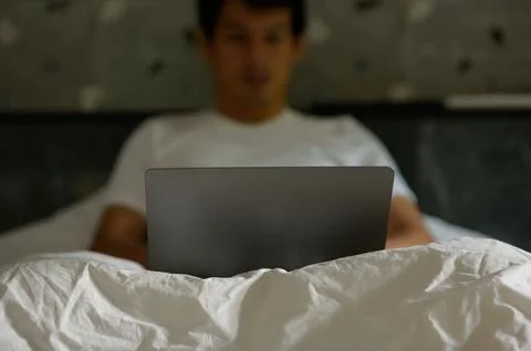 Man Using Laptop in Bed for Work or Leisure at Home Stock Photos
