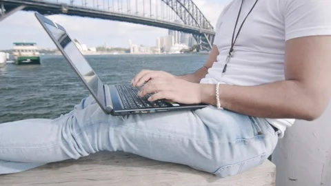 Man Using Laptop on Bench by Sydney Harbour Bridge. Medium Crane Shot Stock Footage 129363764