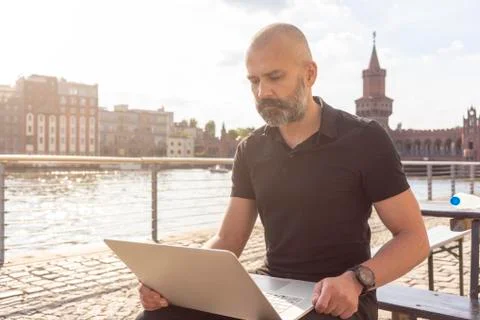 Man using laptop on bridge, river, Oberbaum bridge and buildings in background, Stock Photos