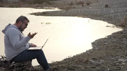 Man using laptop by coast lake. Adult man is holding laptop on his knees Stock Footage 238525968