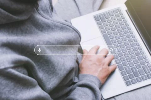 Man using a laptop, with a digital search bar and magnifying glass icon overl Stock Photos