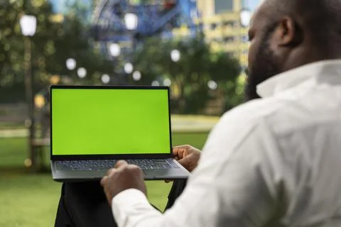 Man using laptop with green screen mockup while sitting in urban park Stock Photos