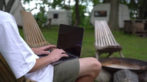 Man using laptop in hammock beside campsite firepit 스톡 동영상 341075813