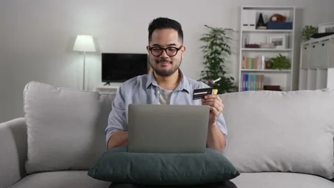 Man using laptop holding credit card for online shopping and payment at home Stock Footage 167940764
