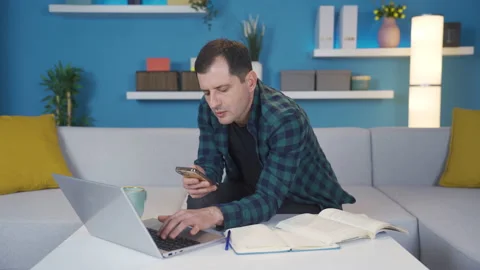 Man using laptop at home looking at his phone, texting, not wanting to work. Vídeo Stock 233117033