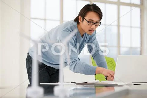 Man Using Laptop With Models Of Wind Turbines On Desk