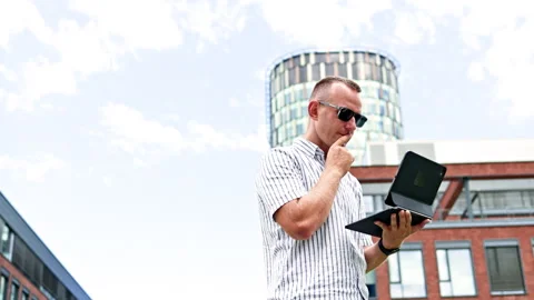 Man using a laptop outside office buildings during the day Stock Footage 348703402