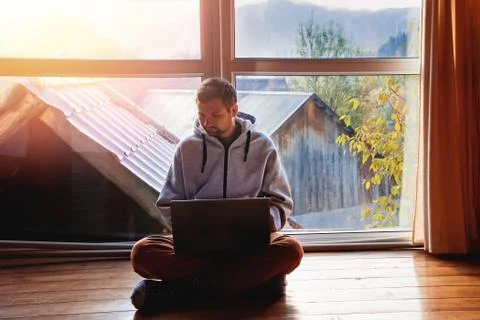 Man using laptop sitting on the floor near big window Stock Photos