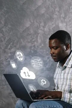 Man using laptop with technology icons on the wall during a work session in a Stock Photos