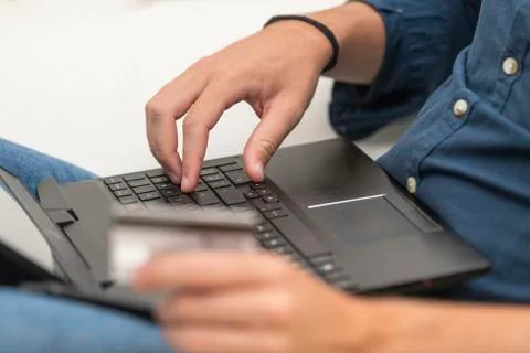 A man using a laptop while holding an out of focus credit card. Commerce and  Stock Photos
