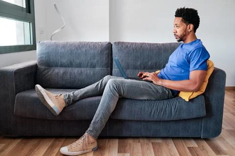 Man using a laptop while sitting on a sofa at home. Stock Photos