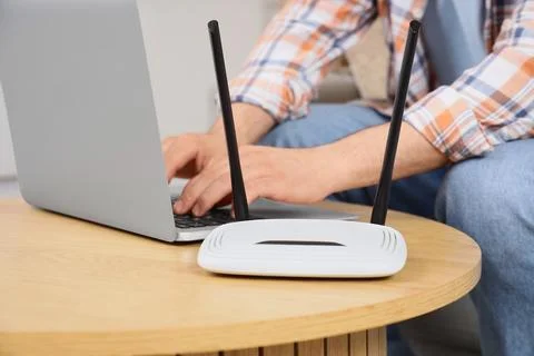 Man using a laptop with a white wi-fi router on a wooden table, internet conn Stock Photos