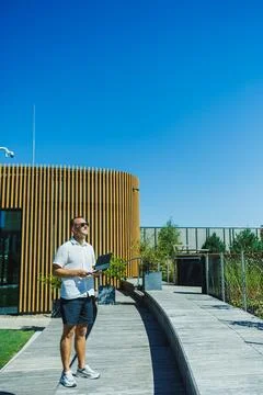 Man using a laptop on a wooden pathway in a modern outdoor space with clear.. Stock Photos