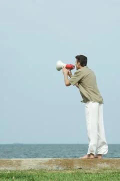 Man using megaphone, facing ocean horizon, full length Stock Photos