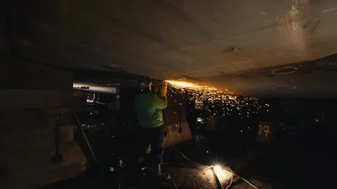 Man using a metal grind on the under side of an old ship with sparks flying Stock Footage 260789216