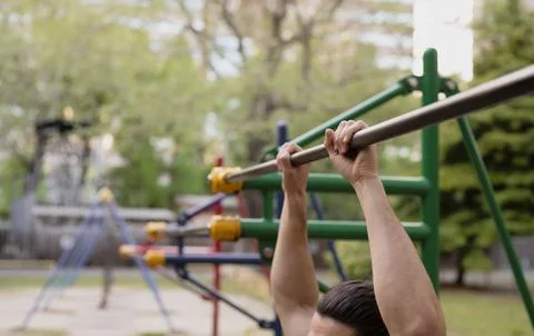 Man using metal pull-up bar at outdoor fitness park Stock Photos